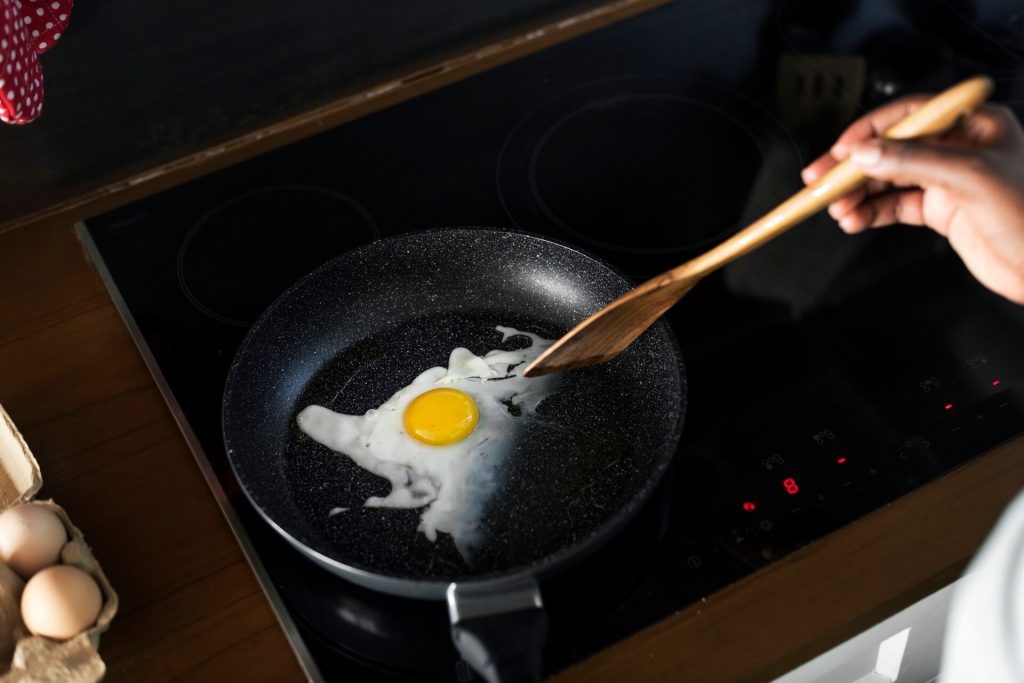 Ägg steks i en svart stekpanna på induktionshäll med träspade