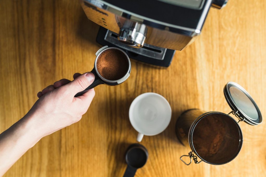 Hand sätter filterhållare med malet kaffe i en espressomaskin på träbänk