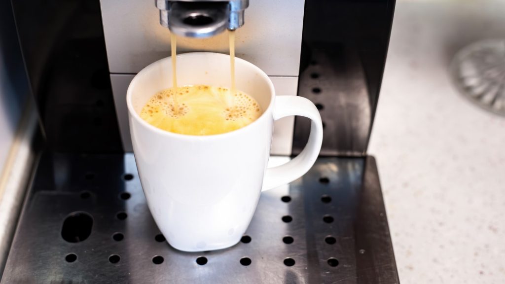 Kaffemaskin brygger kaffe direkt ner i en vit kopp på droppbrickan