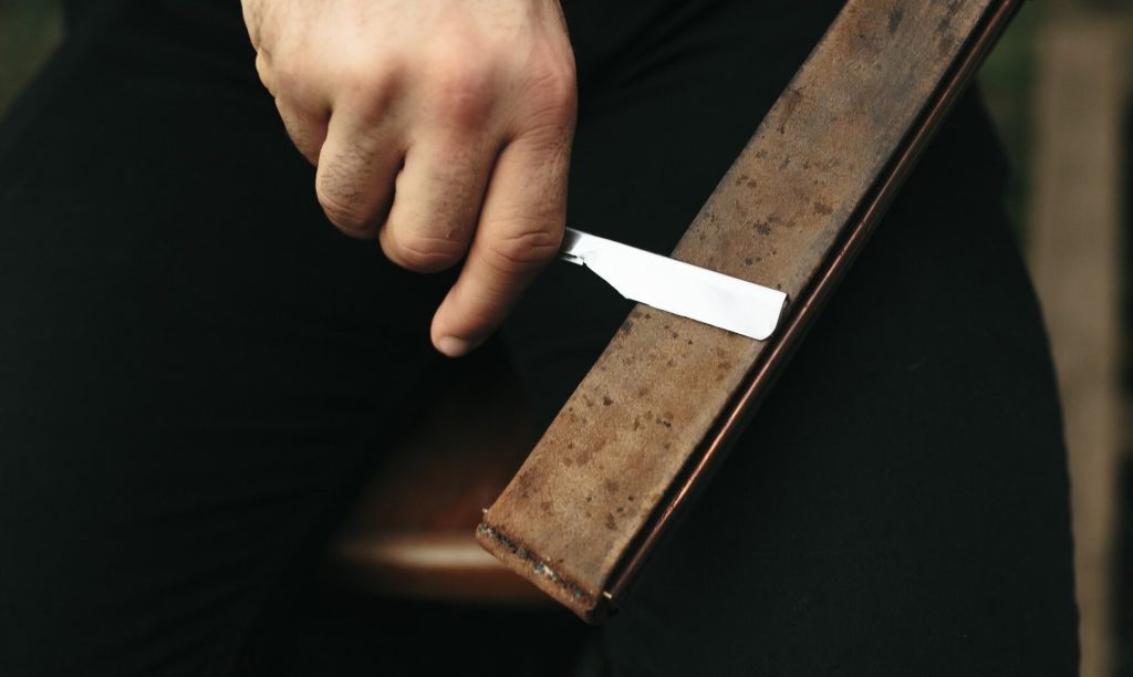 Hand drar ett knivblad mot en lång slipsten mot mörk bakgrund