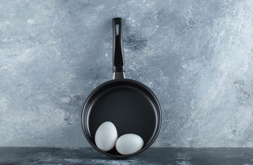 Svart stekpanna med non-stick-yta och två ägg mot en grå vägg